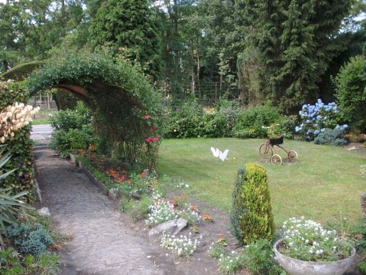 Beautiful garden at Moerkantheide bed and breakfast in Essen, Antwerp, Belgium with green arches and colorful flowers.
