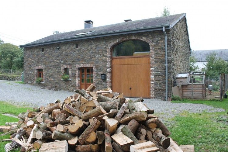 Vakantiehuis Het Huis Hiernaast in Houffalize, Ardennen, met houtstapel op de voorgrond.