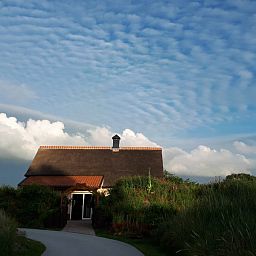 Pittoresk uitzicht op Duinrand Vakantievilla's Type 2 in De Koog, Texel, omgeven door weelderige natuur en wolkenlucht.
