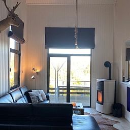 Comfortabele woonkamer in Dogo In Paradise vakantiehuis, Houffalize, Ardennen, met grote ramen en houtkachel.