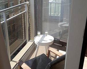 Zonnig balkon van T ZAND appartement, Oostduinkerke, met zitje en uitzicht op de omgeving, perfect voor ontspanning.