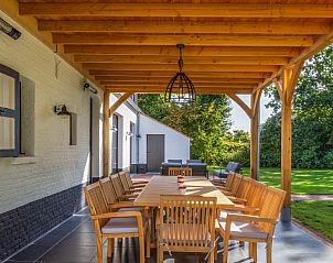 Overdekt terras van Mushoeve vakantiehuis in Zoersel, Antwerpen met houten eettafel en uitzicht op tuin.