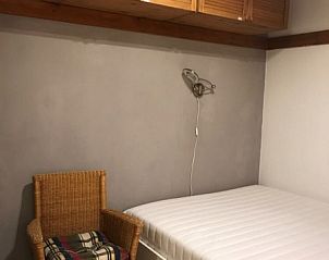 Rustieke slaapkamer in Residence Reine Blanche, Val Thorens, voorzien van warme houten elementen en een uitnodigende rieten stoel.