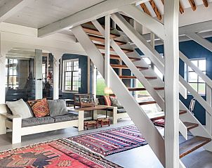 Open trap in Vakantiehuisje in Piaam leidt naar de bovenverdieping, met kleurrijke tapijten en comfortabele zitplaatsen.