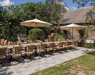 Buitenterras van Les Trois Sangliers vakantiehuis, Chanly, Ardennen, met lange tafels en stoelen onder de zon.