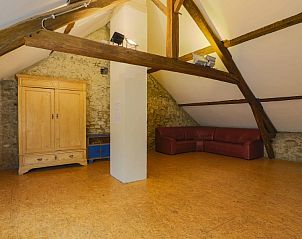 Ruime zolderkamer in Les Trois Sangliers vakantiehuis, Chanly, Ardennen, met houten vloer en comfortabele bank.