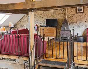 Zithoek met televisie in Les Trois Sangliers vakantiehuis, Chanly, Ardennen, met rustieke stenen muren.