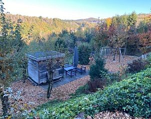 Uitzicht op de tuin en heuvels vanuit Dogo In Paradise vakantiehuis, Houffalize, Ardennen, omgeven door herfstkleuren.