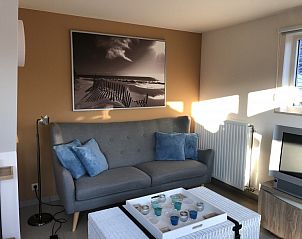 Gezellige woonkamer in vakantiehuis Zee en Polder, Westende, Belgische kust, met comfortabele bank en kunst aan de muur.