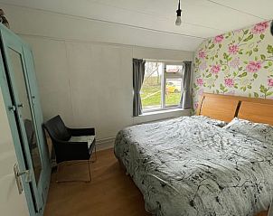 Sfeervolle slaapkamer in Huisje in De Westereen op het Friese platteland, met bloemenbehang en uitzicht op de groene omgeving.