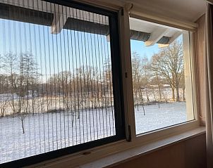 Uitzicht op besneeuwd landschap vanuit slaapkamer in Huisje in Oldenzaal vakantiehuis in Twente, Overijssel.